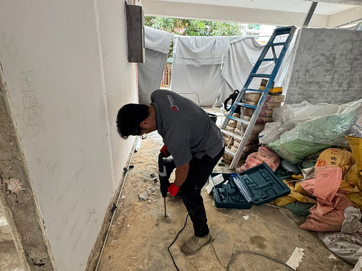 Technician applying soil termiticide barrier treatment around a Singapore home foundation